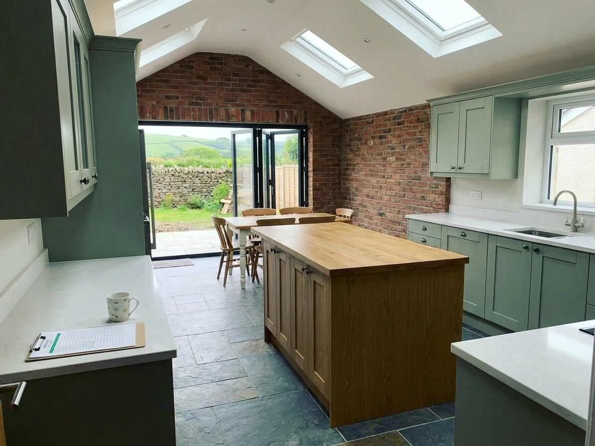 Kitchen with green cabinets, butcher block island, stone wall, and glass doors to a garden.