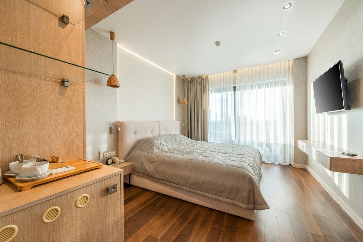 Modern hotel room with a bed, TV, and wooden furniture.