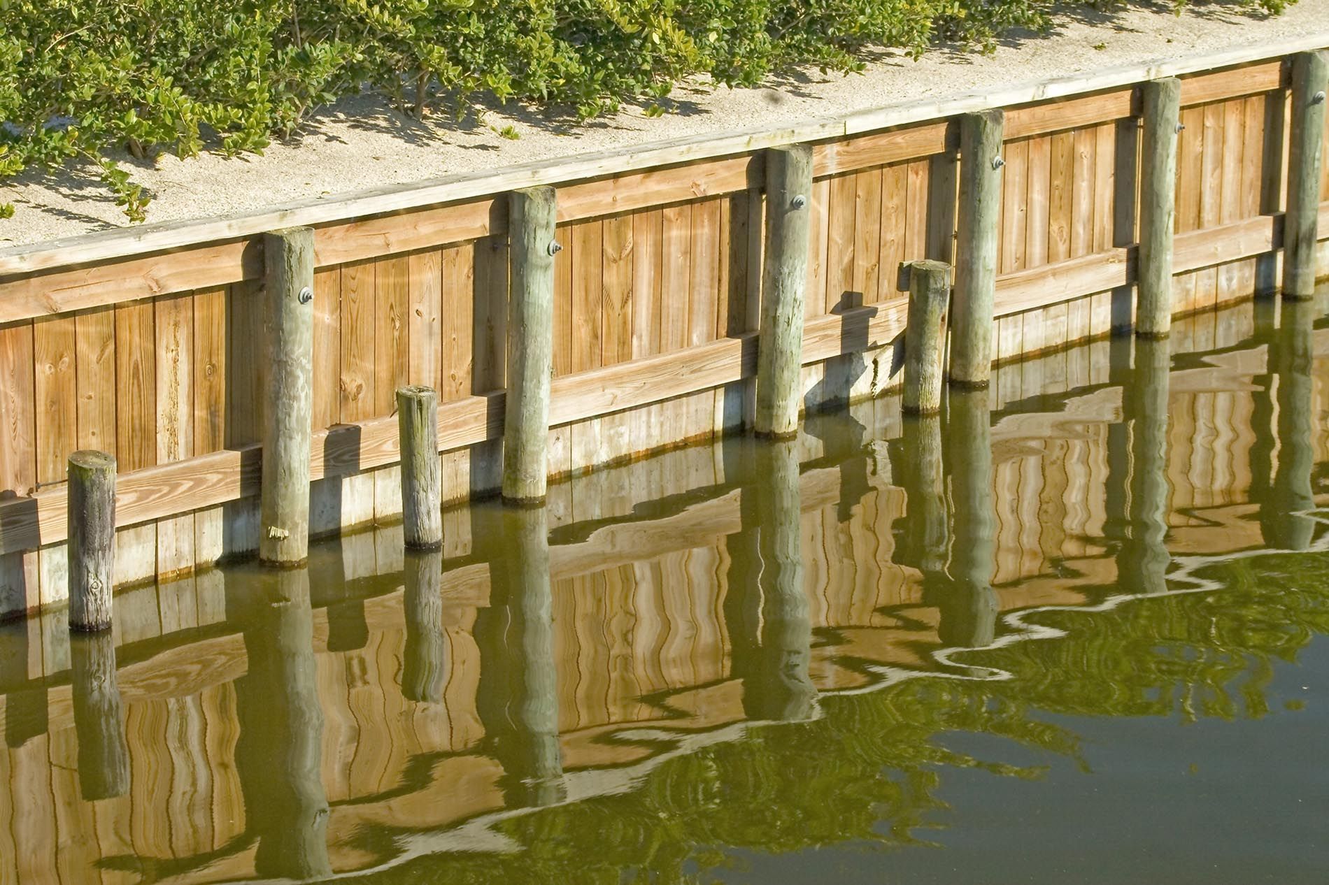 A wooden wall along a body of water with a reflection in the water.