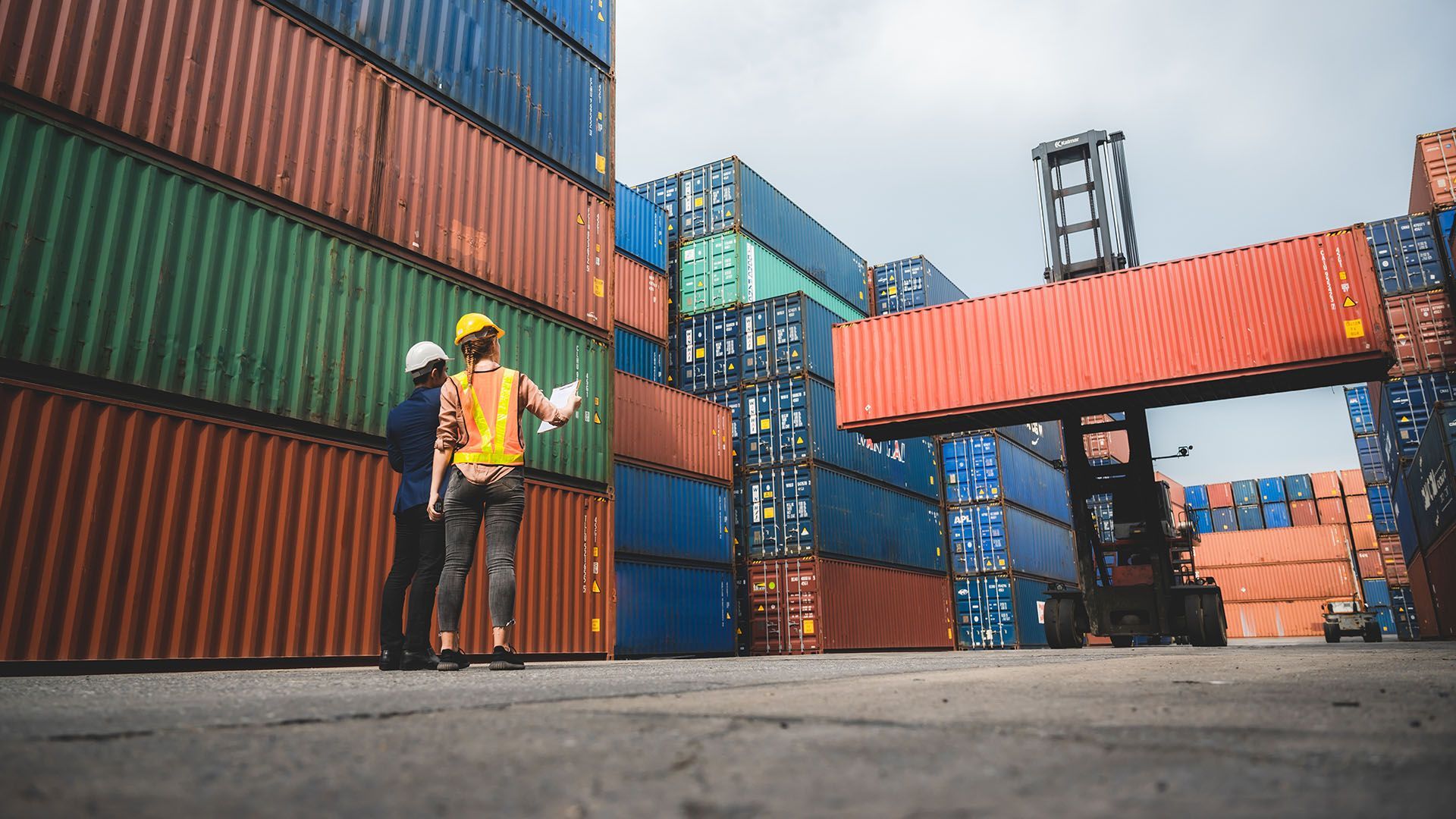 Two men are standing in front of a stack of shipping containers.