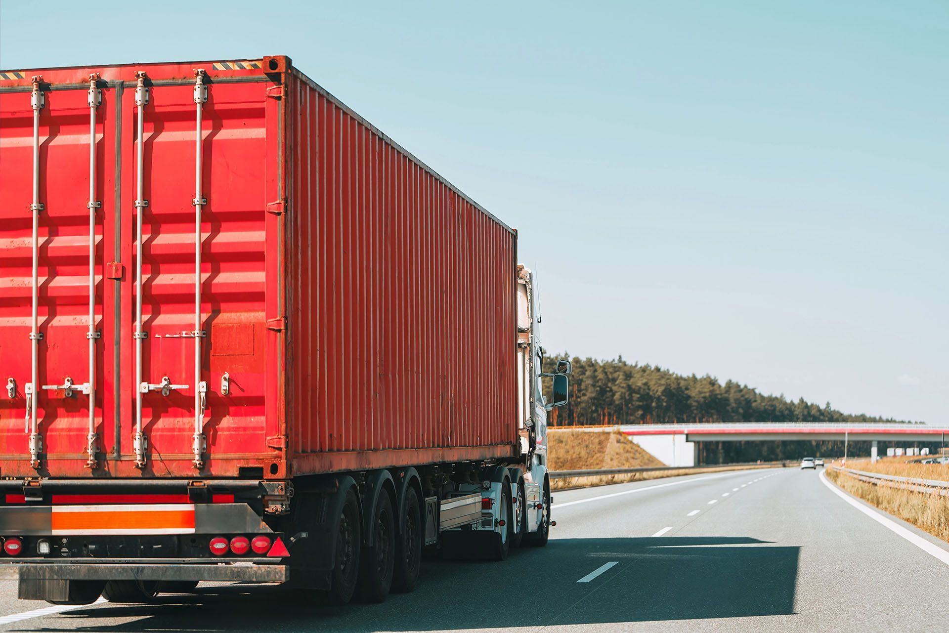 Red semi-truck with cargo container drives on highway.