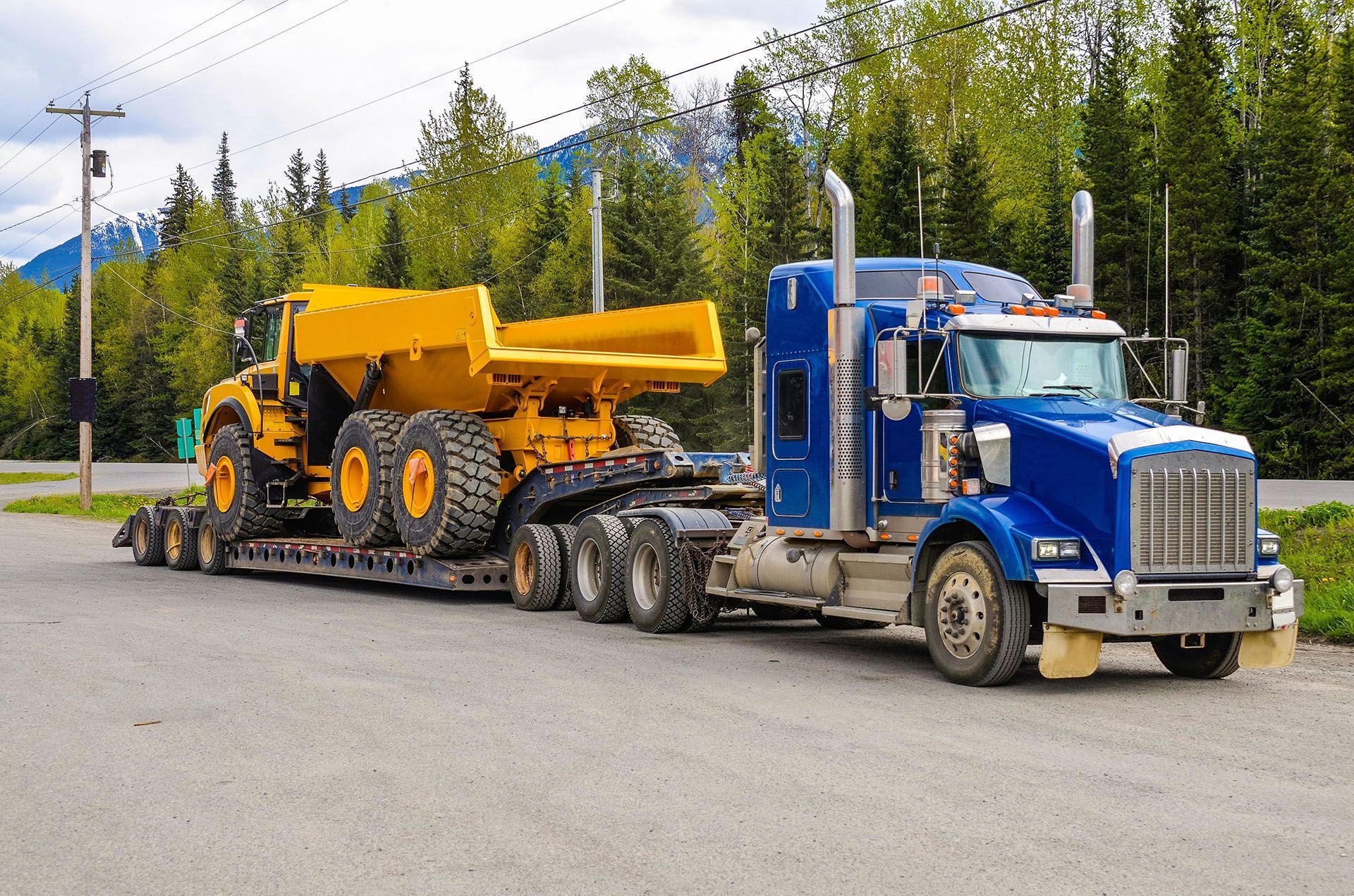 Blue semi-truck hauling a large yellow construction dump truck.