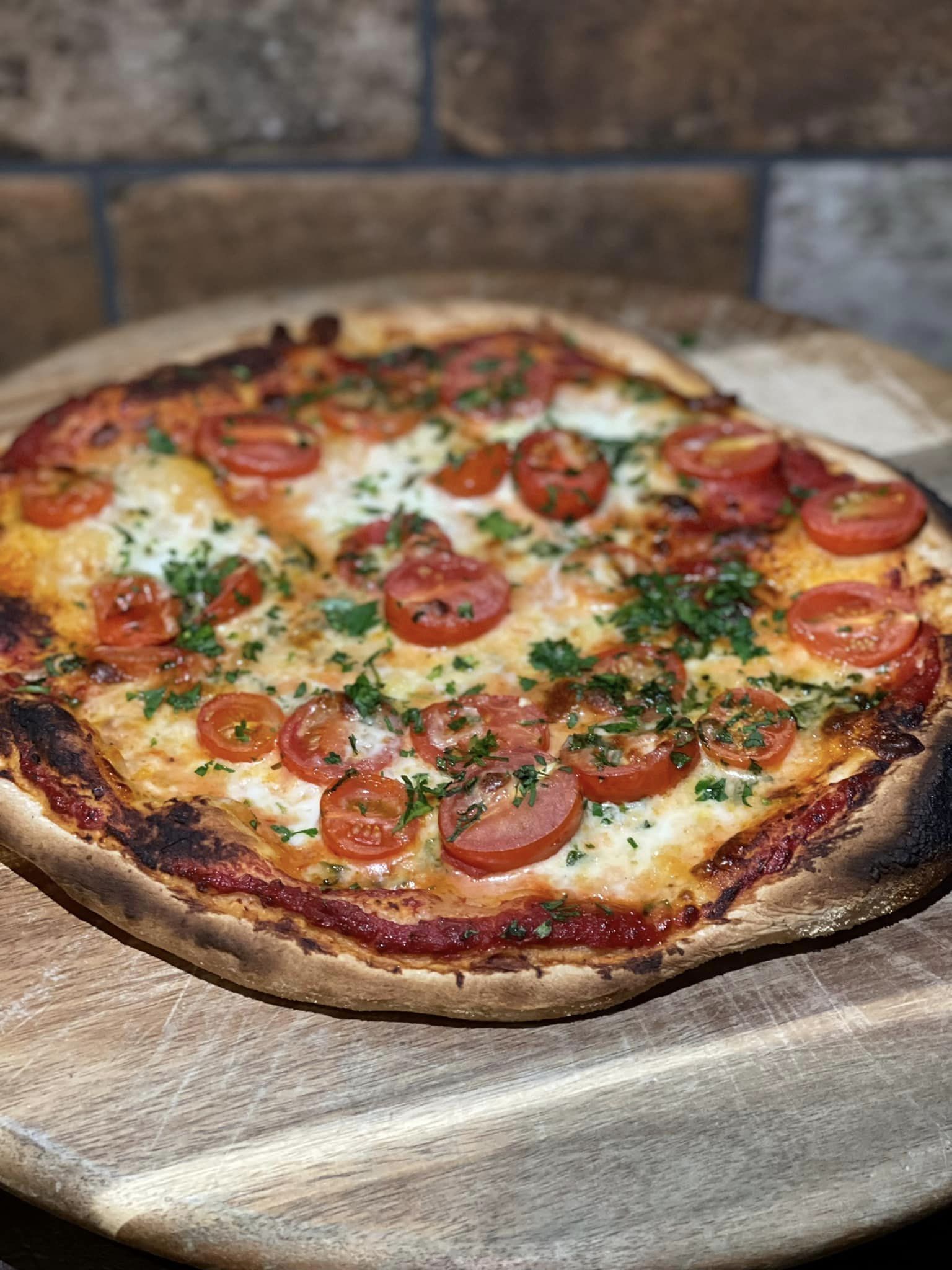 A Pizza With Tomatoes And Cheese On A Wooden Cutting Board — Original North Australian in Bowen, QLD