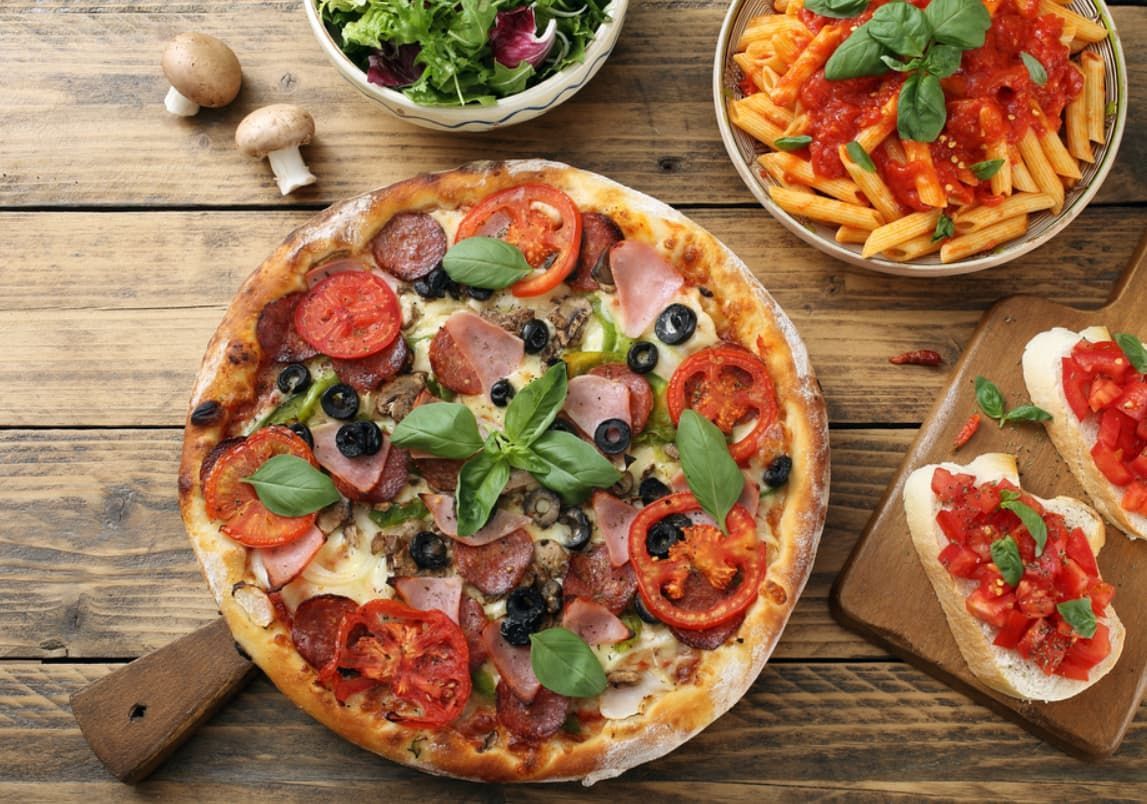 A Pizza Is Sitting On A Wooden Table Next To A Bowl Of Pasta And A Salad — Original North Australian in Bowen, QLD
