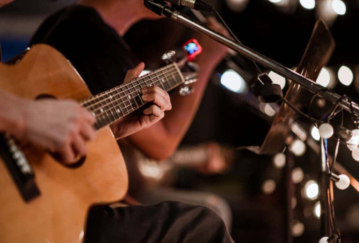 A Man Is Playing An Acoustic Guitar In Front Of A Microphone — Original North Australian in Bowen, QLD