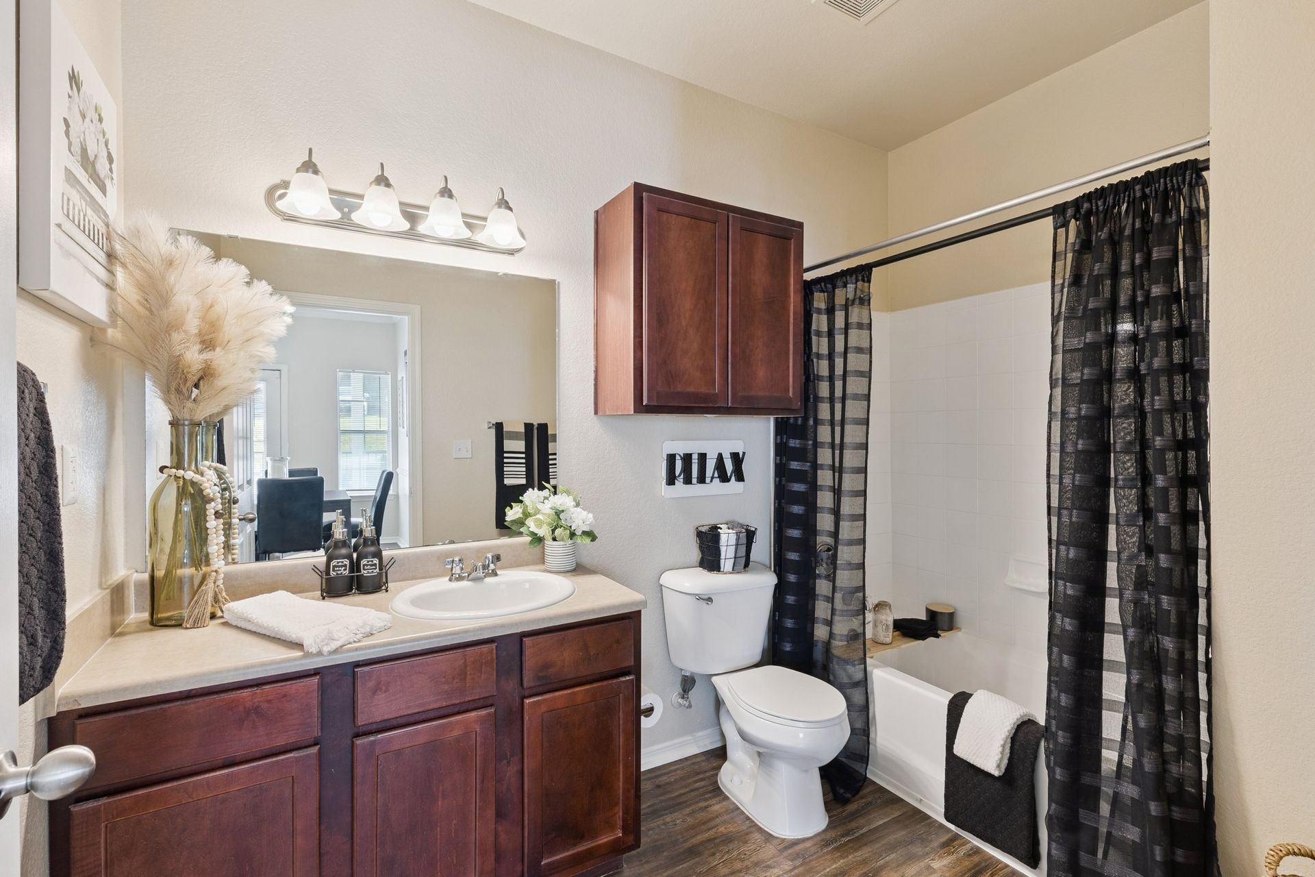 Bathroom with dark wood vanity and cabinet, white sink, toilet, and bathtub with black curtain.