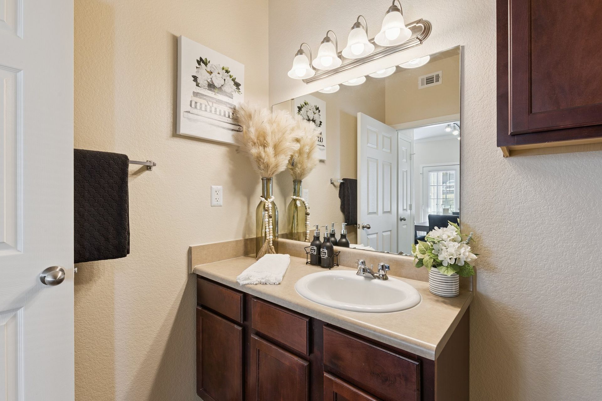 Bathroom with vanity, sink, mirror, and decorative items. Brown cabinets and light fixtures.