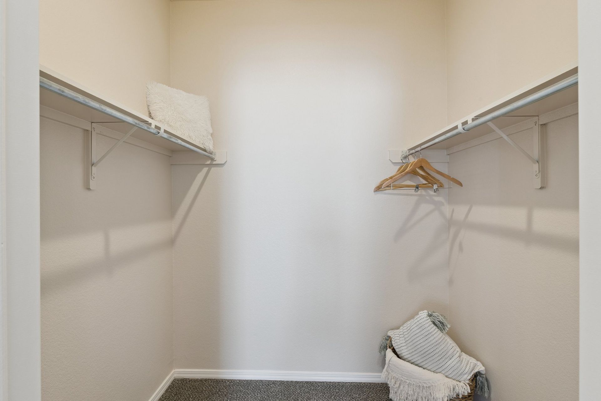 Empty walk-in closet with white shelves, beige walls, and carpeted floor; a few hangers and blankets.