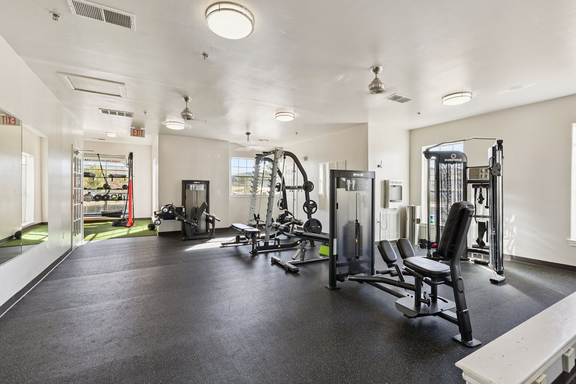 Gym with exercise equipment, including weight machines and mirrors. Black flooring and white walls.
