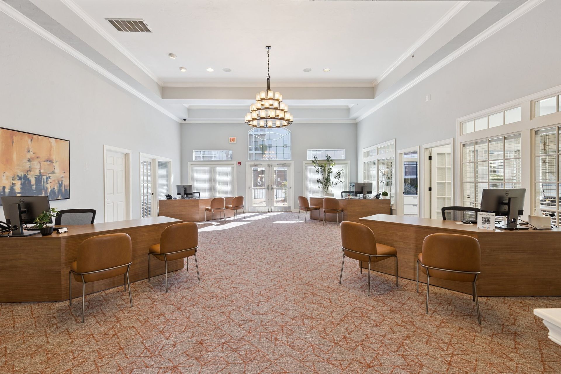 Reception area with desks, chairs, and a chandelier; light-colored walls and carpet.