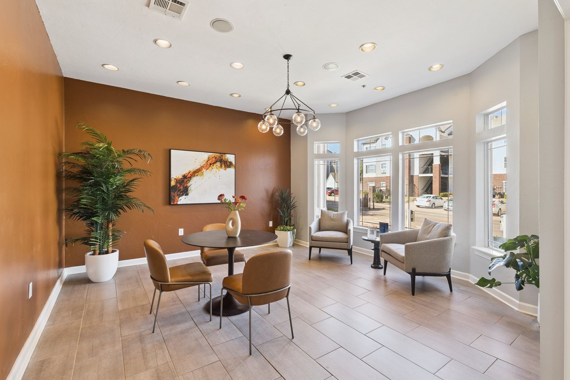 Bright waiting area with seating, round table, artwork, brown accent wall, and large windows.