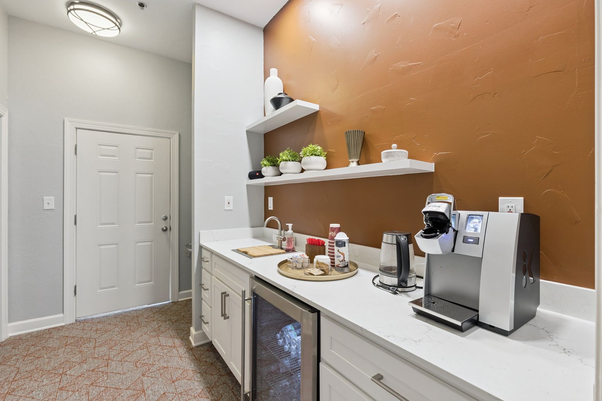Coffee bar with built-in cabinetry, espresso machine, wine fridge, shelves with decor, and a textured orange wall.
