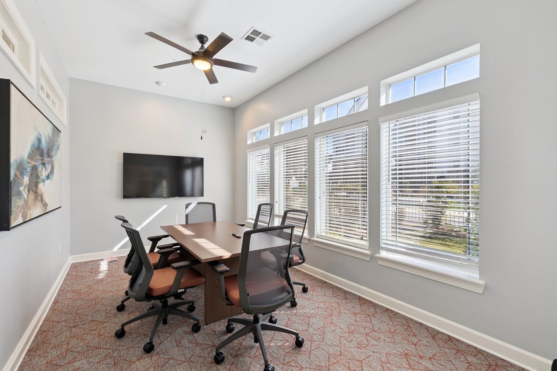 Meeting room with table, chairs, TV, windows, and ceiling fan.