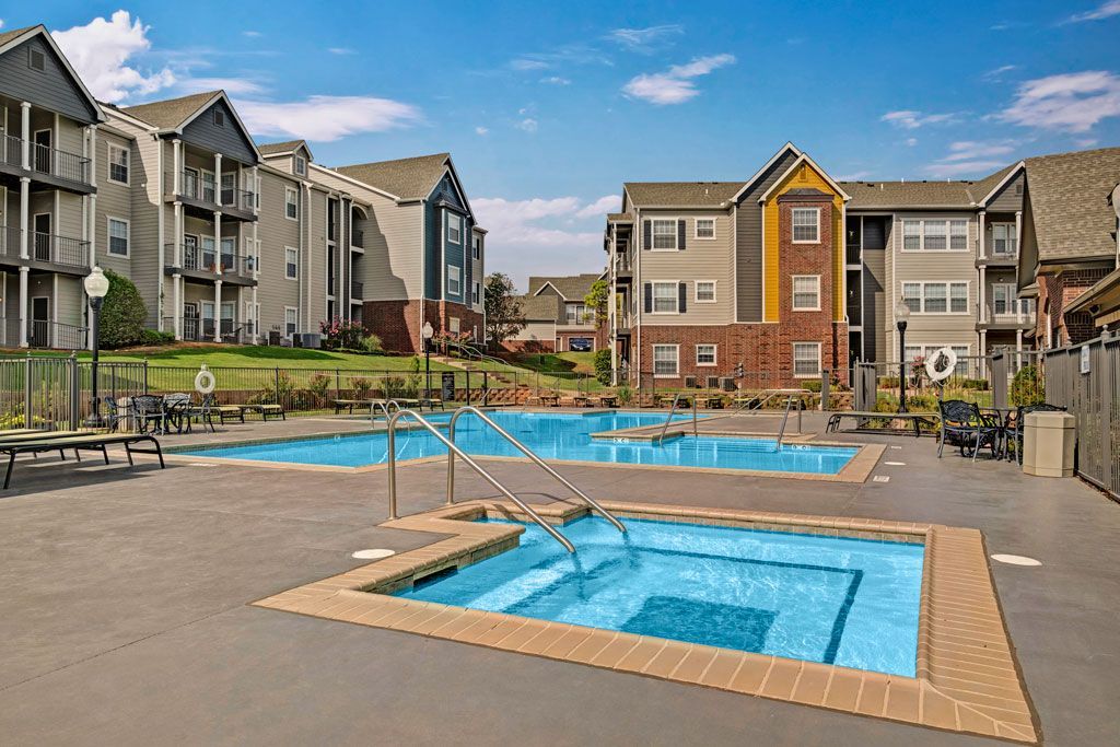 Apartment complex with a pool and hot tub on a sunny day.