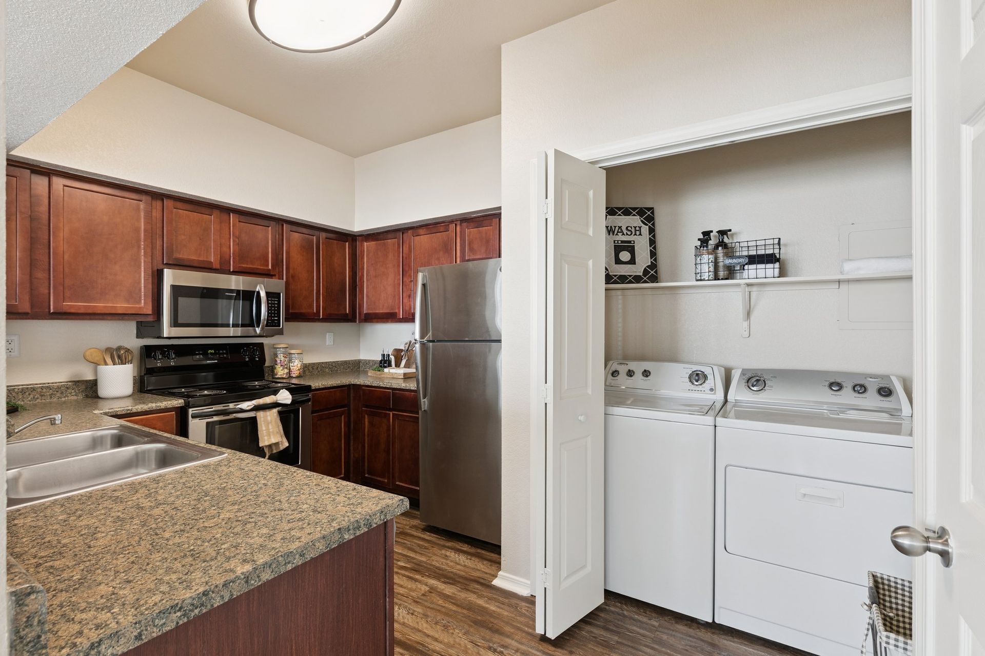 Kitchen with dark wood cabinets, stainless steel appliances, and laundry machines in a closet.