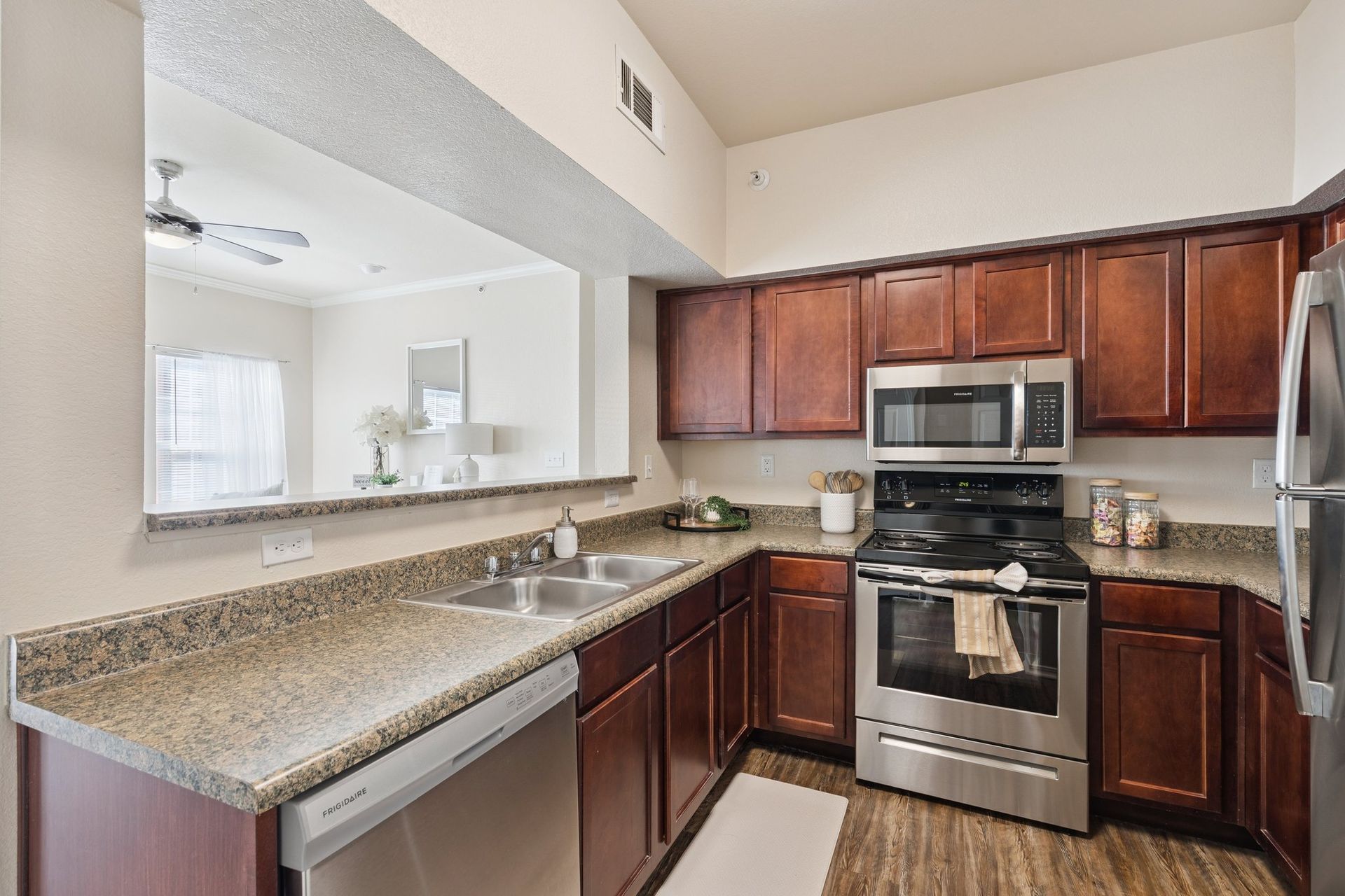Kitchen with dark wood cabinets, stainless steel appliances, and a pass-through to the living area.