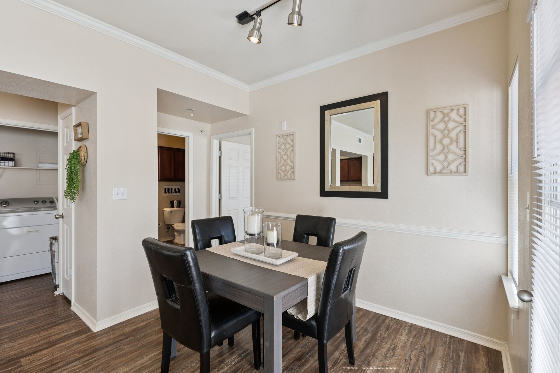 Dining room with gray table, black chairs, mirror, decor, and doorway to a laundry room.