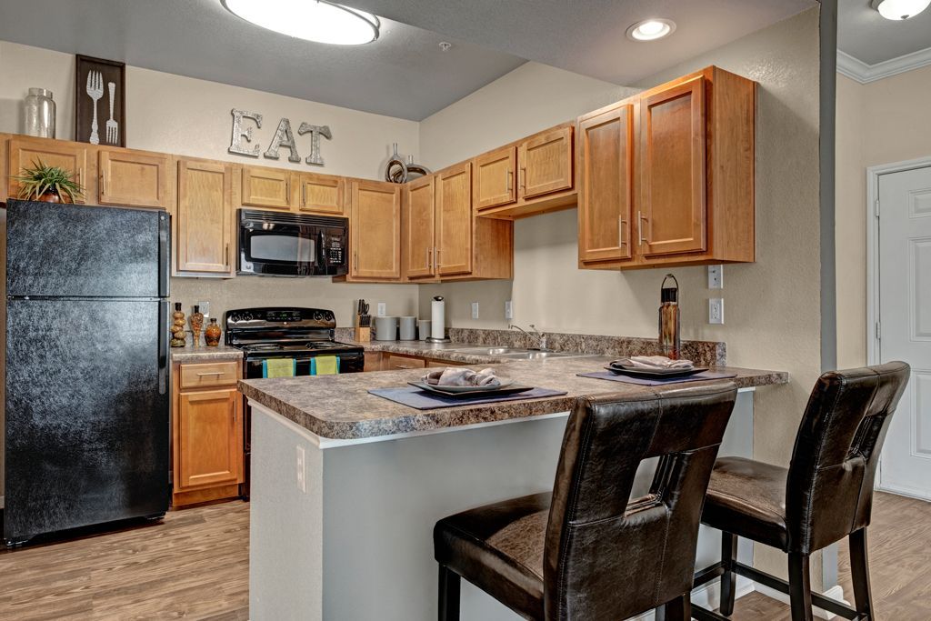 A kitchen with wooden cabinets , a black refrigerator , a stove , and a bar.