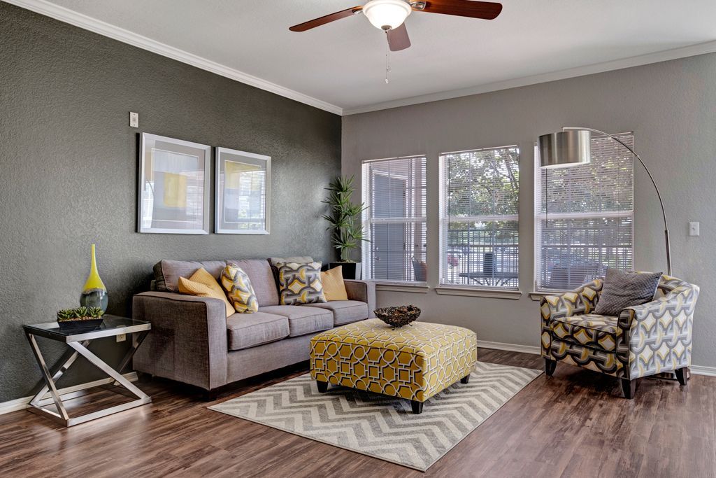A living room with a couch , chair , ottoman and ceiling fan.