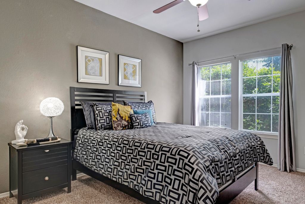 A bedroom with a bed , nightstand , lamp and ceiling fan.