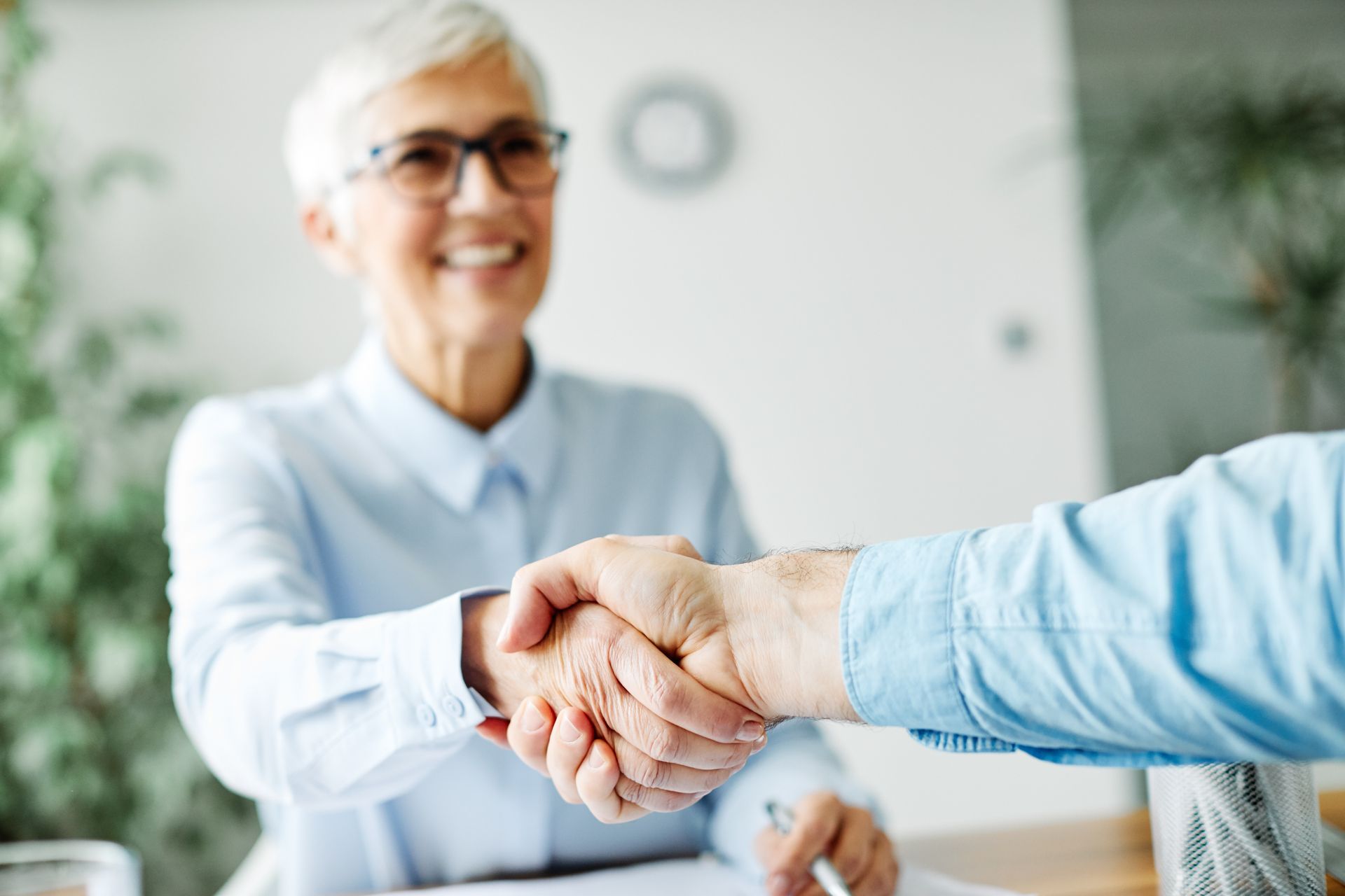 Woman in glasses shakes hands with another person, smiling indoors.