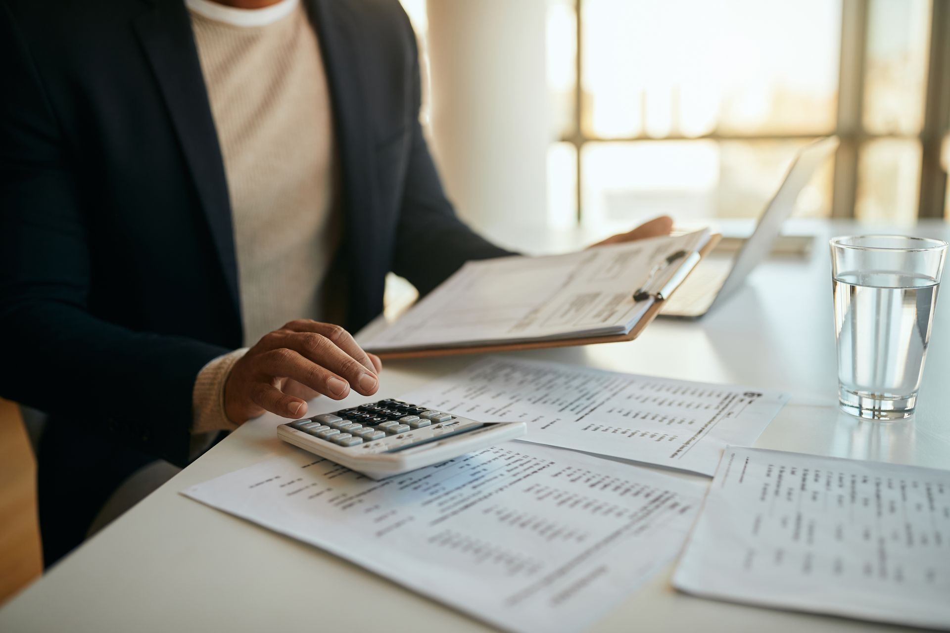 Man in blazer calculating with calculator and papers on a desk.