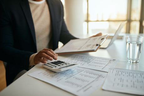 Man in blazer calculating with calculator and papers on a desk.