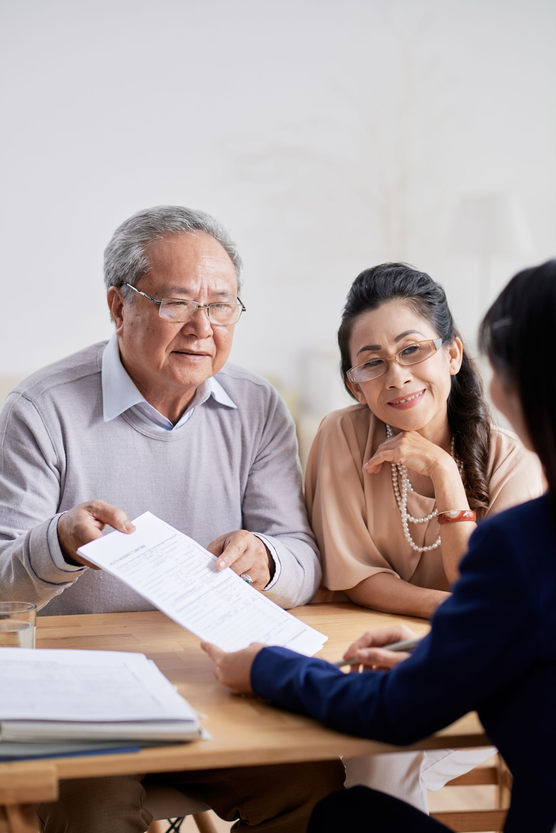 Elderly couple reviewing documents with a financial advisor at a table; man is holding a paper.