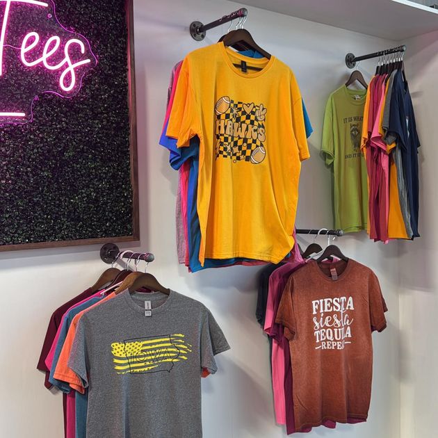 A bunch of shirts hanging on a wall with one that says fiesta meal tequila