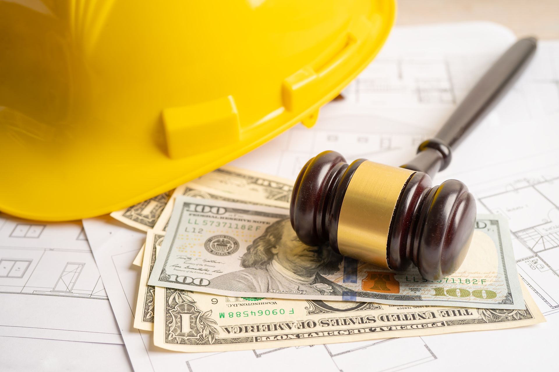 Yellow hard hat, wooden gavel, and cash money on building blueprints.