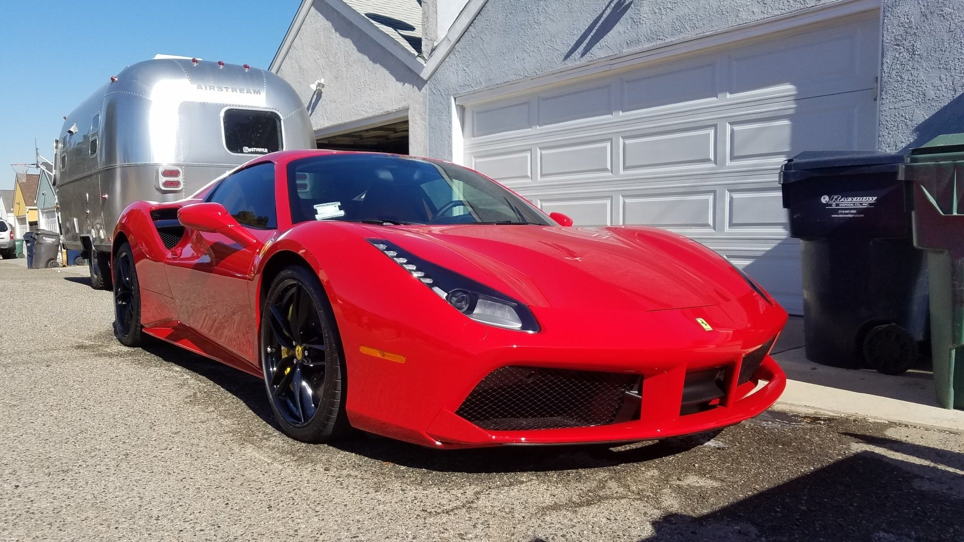 Red Ferrari sports car parked with a silver Airstream trailer in driveway.