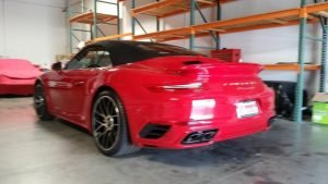 Red Porsche 911 convertible parked inside a warehouse with shelves.
