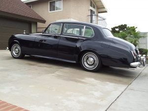 Black classic Rolls-Royce sedan parked on a driveway in front of a house.