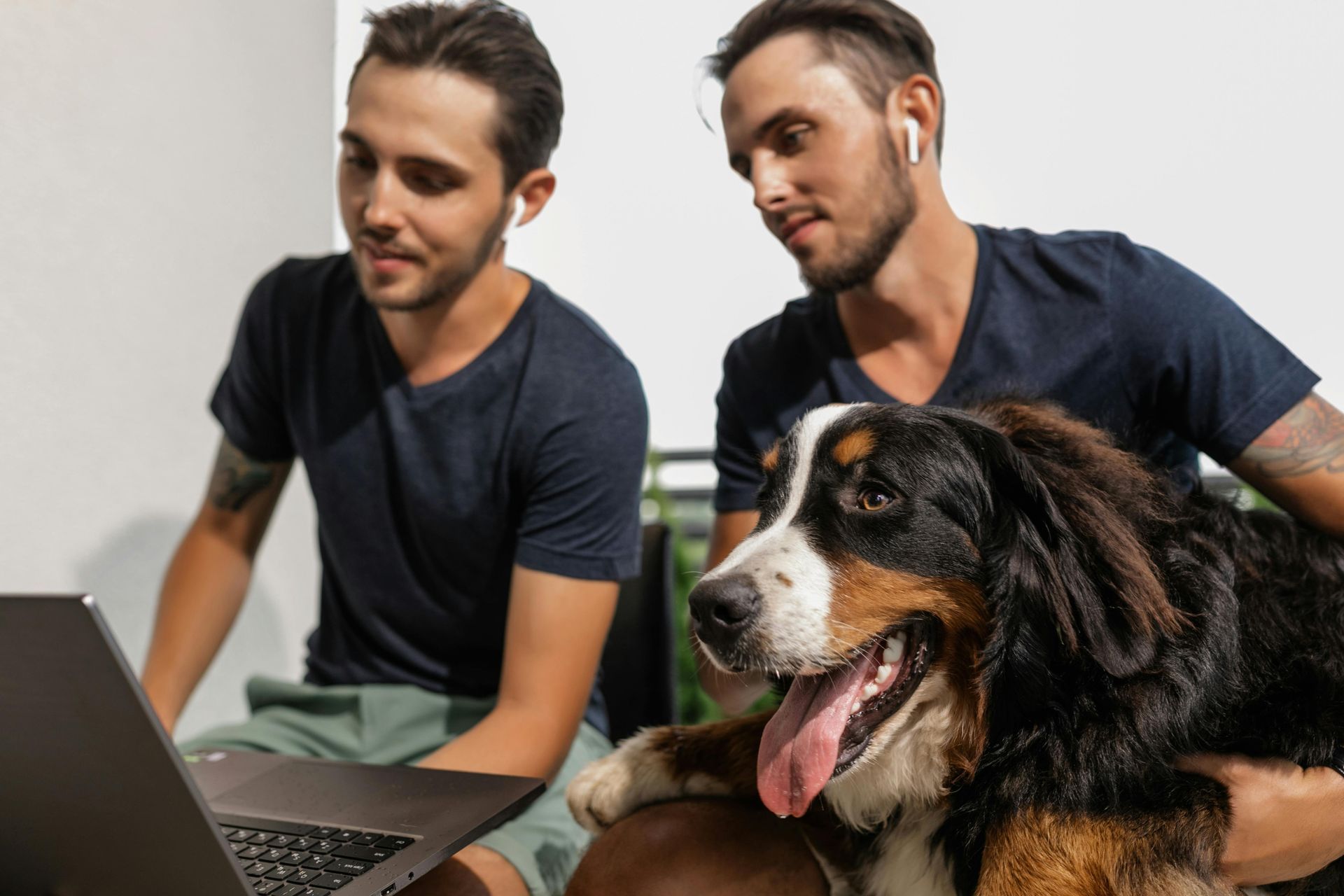 Two men and a dog are sitting in front of a laptop computer.
