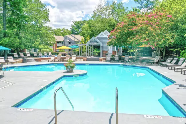Swimming pool area with lounge chairs, gazebo, and lush trees.
