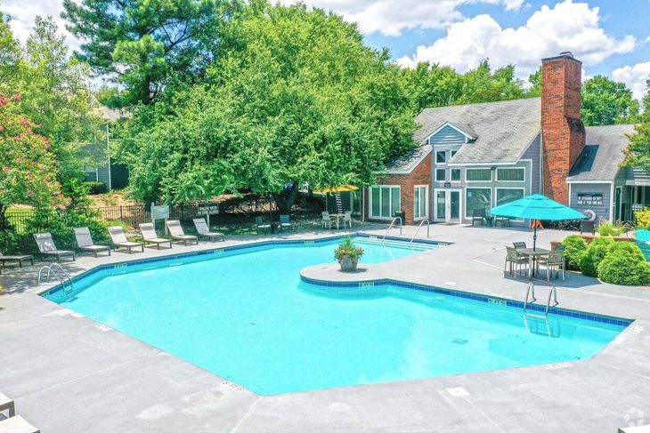 Swimming pool with lounge chairs, tables, and a clubhouse in the background.