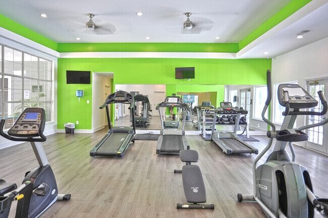 Gym interior with cardio machines; bright green walls and a light-colored floor.
