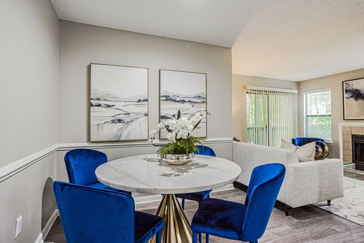 Dining area with marble table, blue velvet chairs, and abstract art; living room in background.