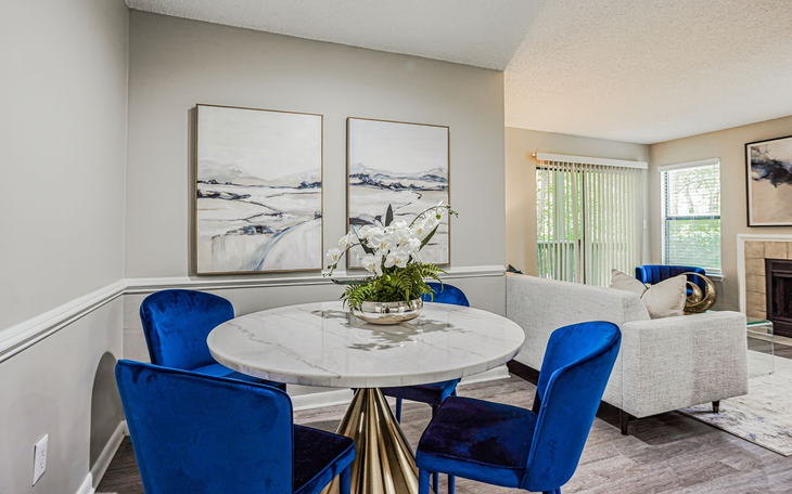 Dining area with marble table, blue velvet chairs, and abstract art; living room in background.