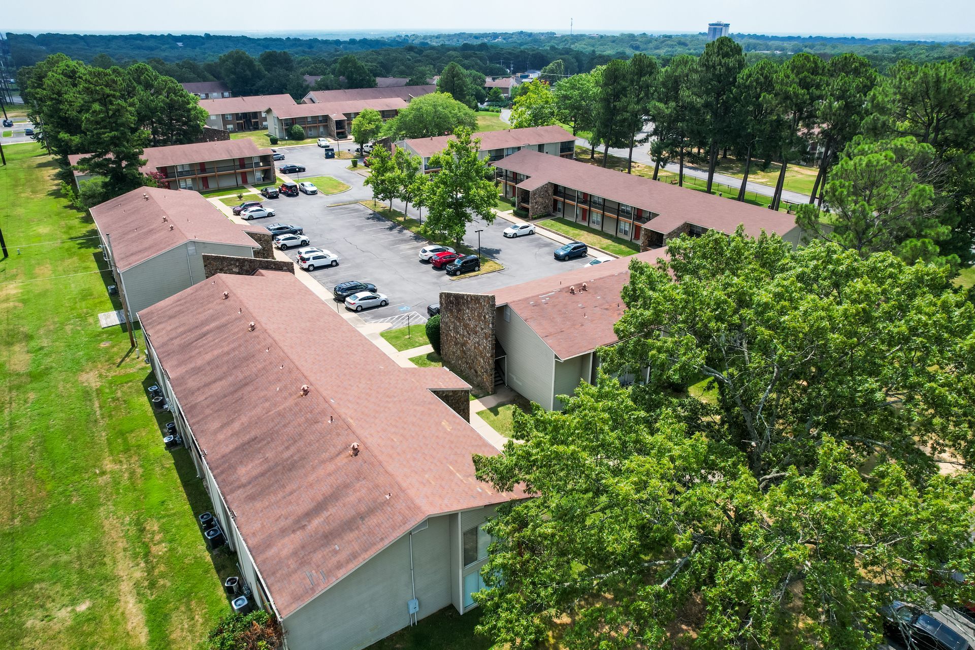 Aerial view of apartment complex with brown roofs, parking lot, and green lawns.