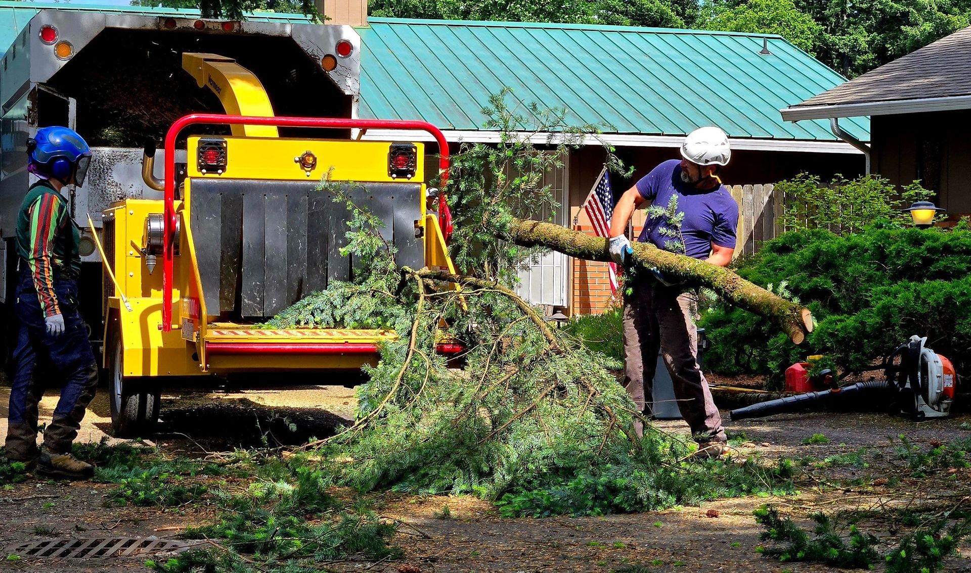 Two men are cutting a tree with a machine in front of a house.