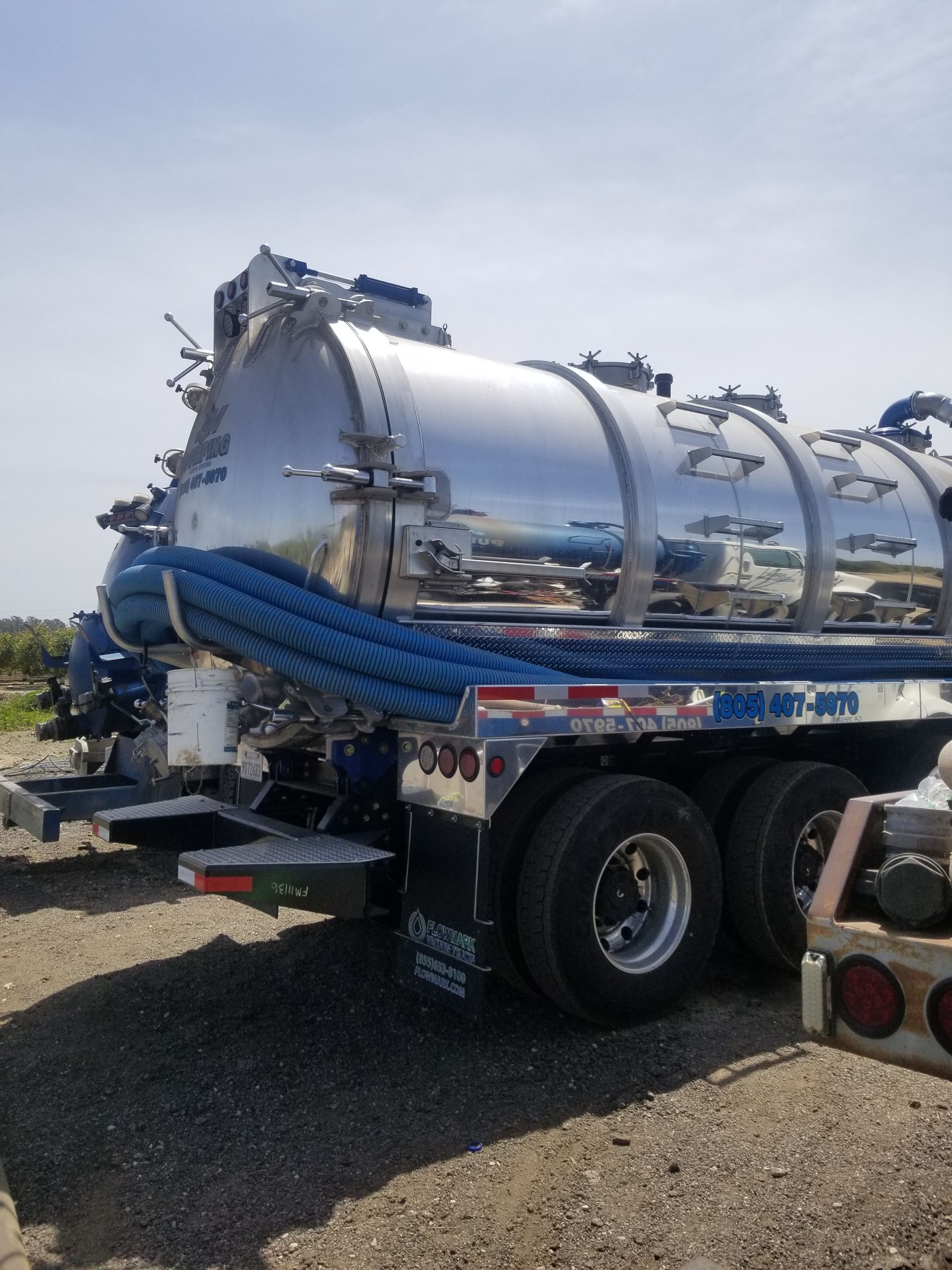 A stainless steel vacuum truck is parked in a gravel lot