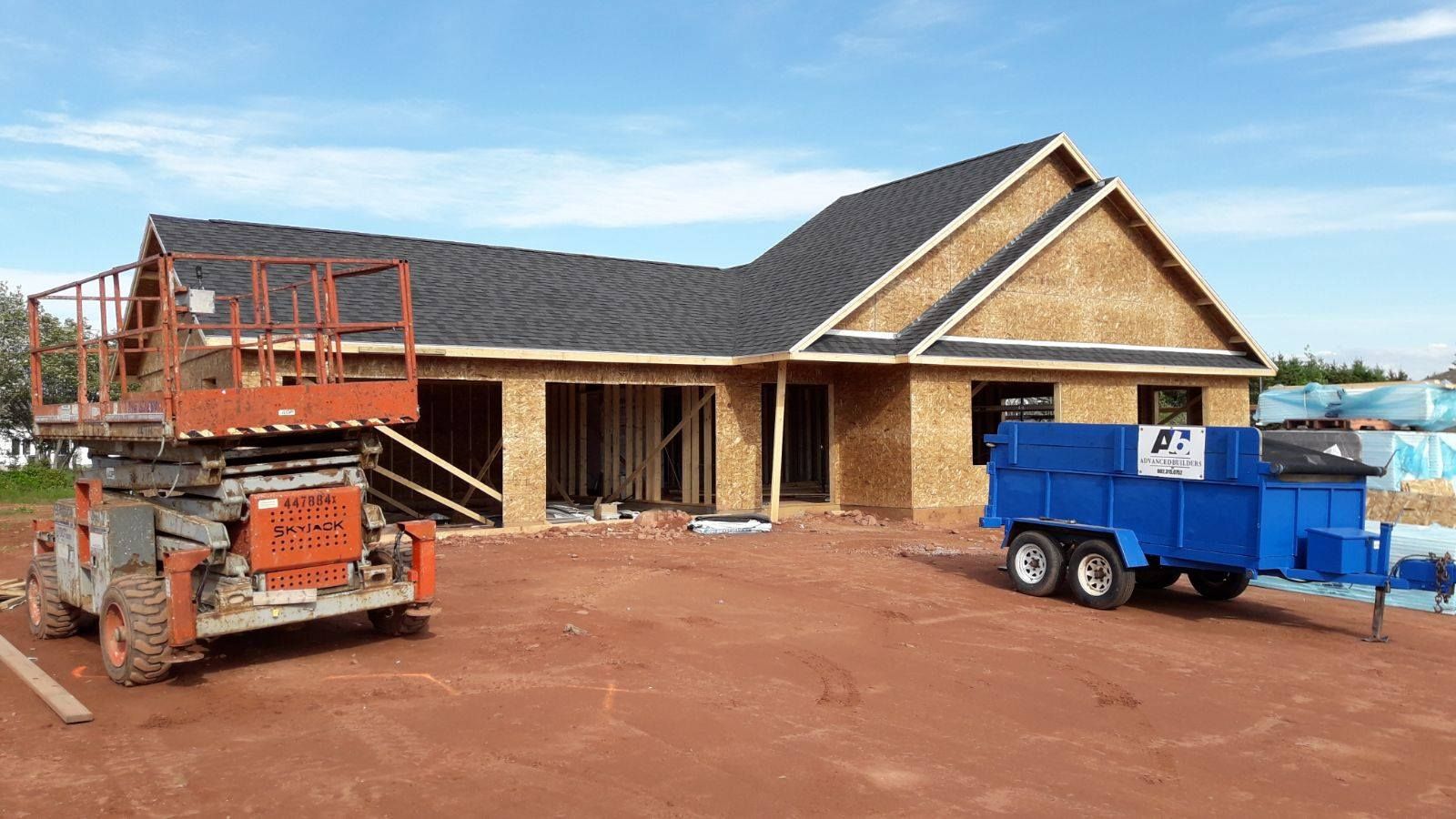 A house is being built and a blue dumpster is parked in front of it.