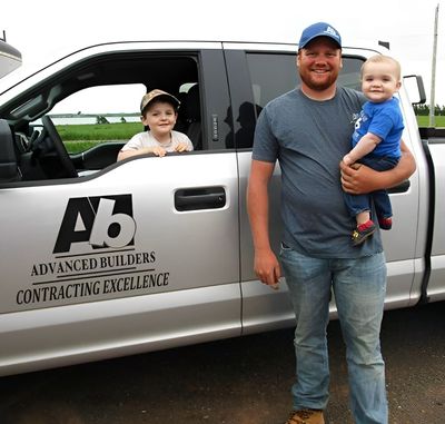 A man holding a baby in front of a truck that says advanced builders contracting excellence