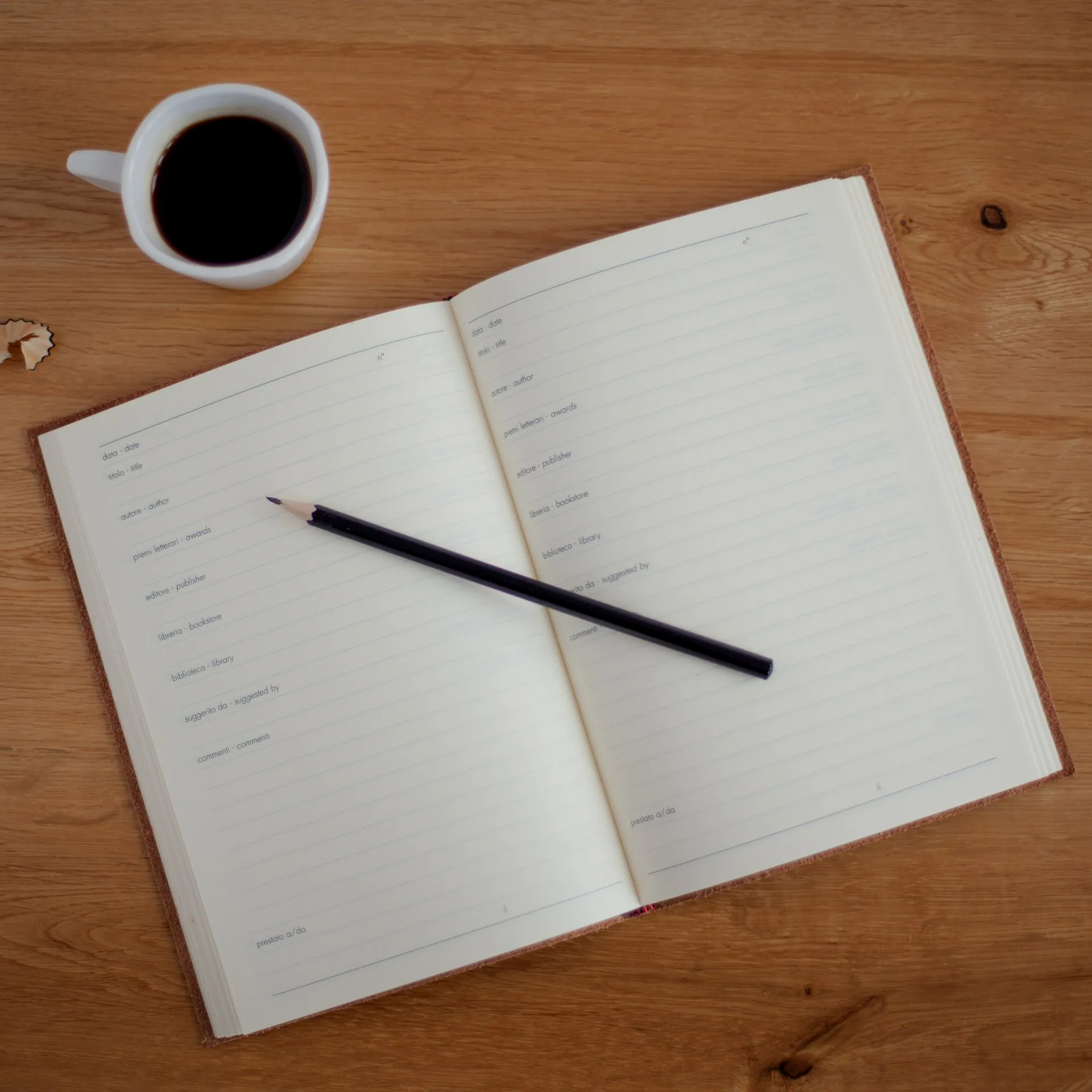 an open notebook with a pencil and a cup of coffee on a wooden table