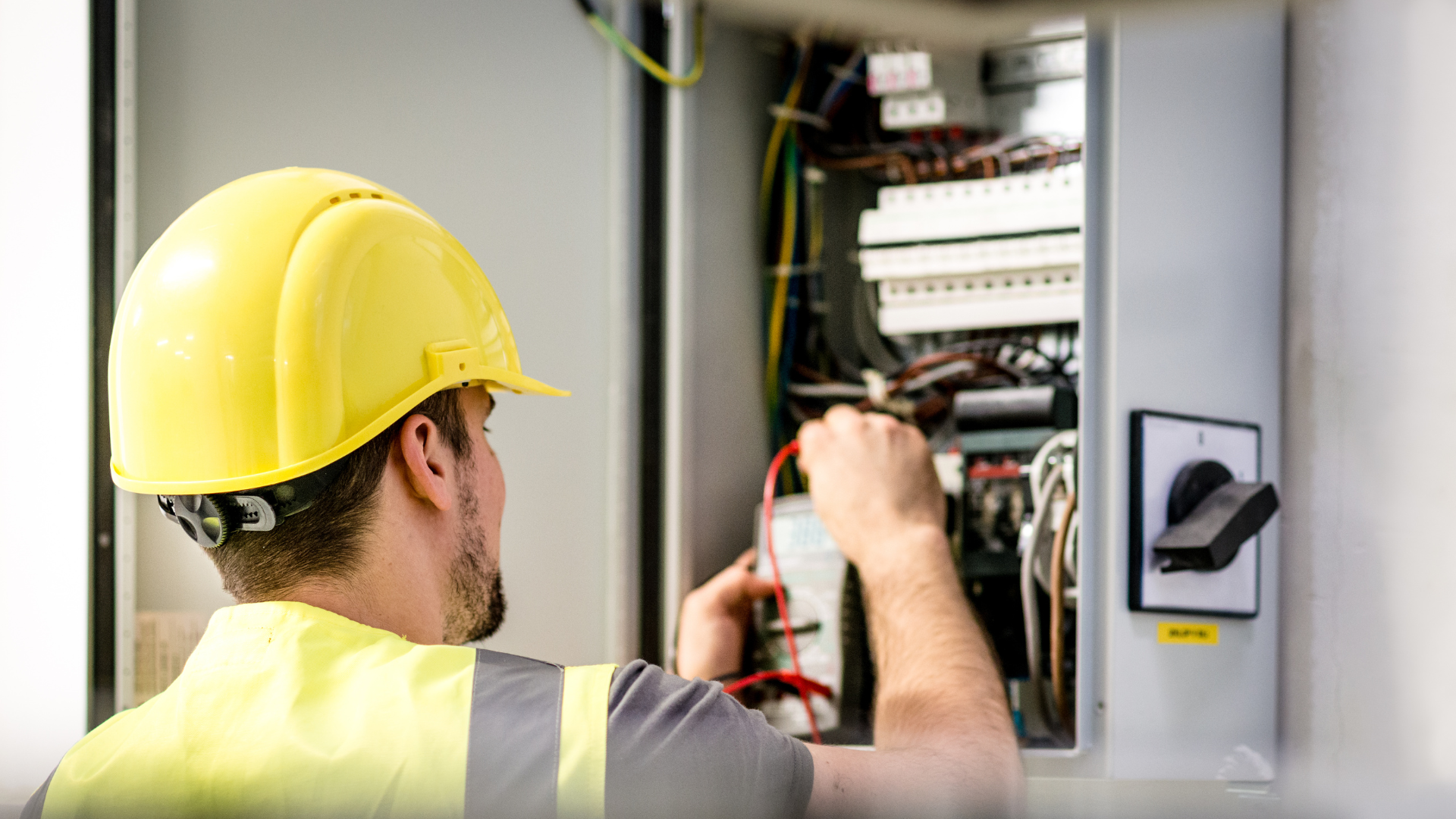 A man wearing a hard hat and safety vest is working on an electrical box.