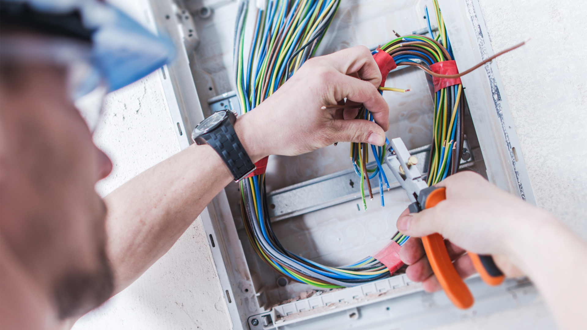 A man is working on an electrical box with a pair of pliers.