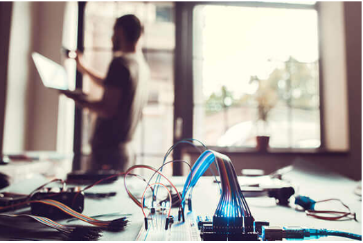 A man is standing in front of a window while using a laptop computer.