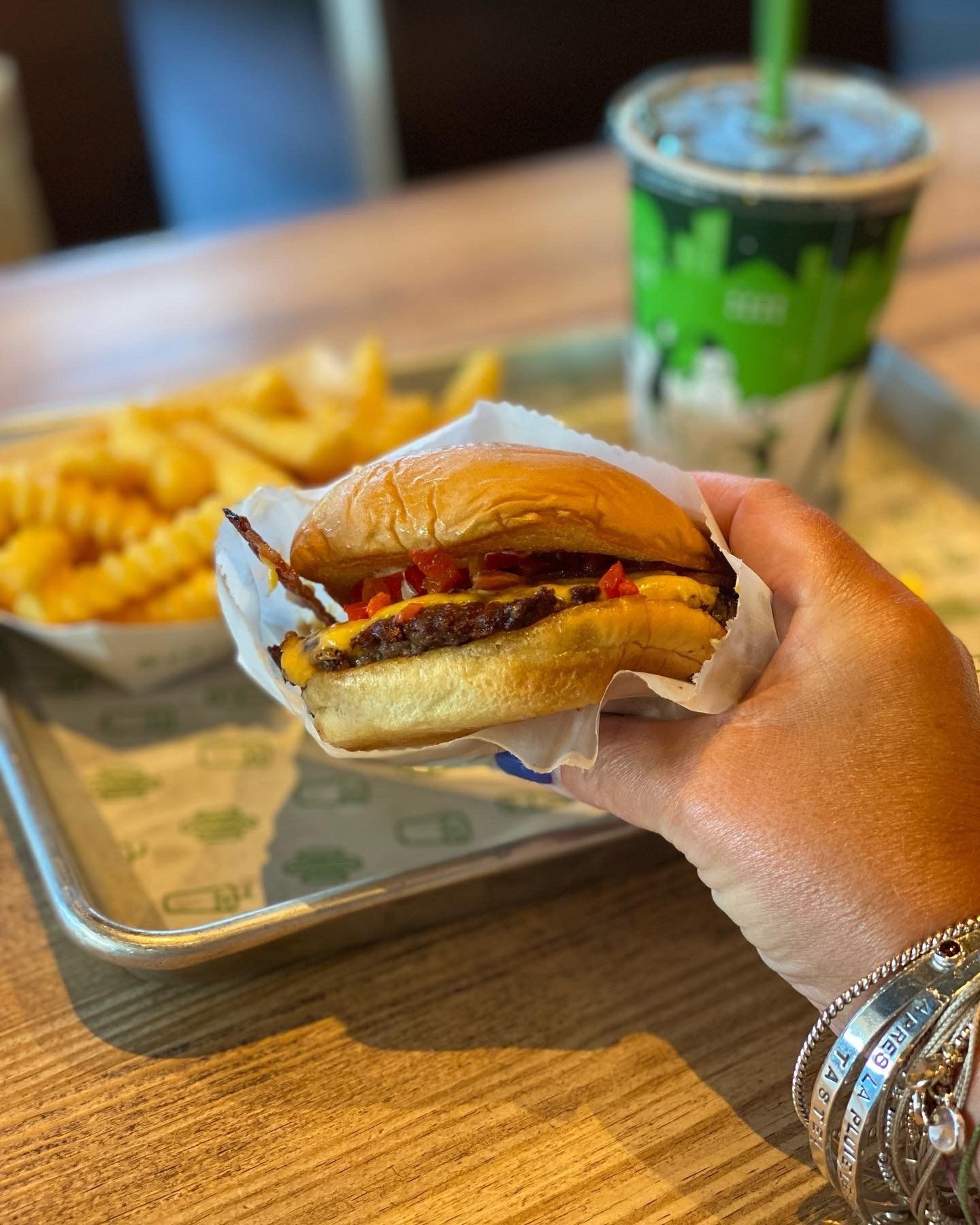 A person is holding a hamburger in front of a tray of french fries and a drink.