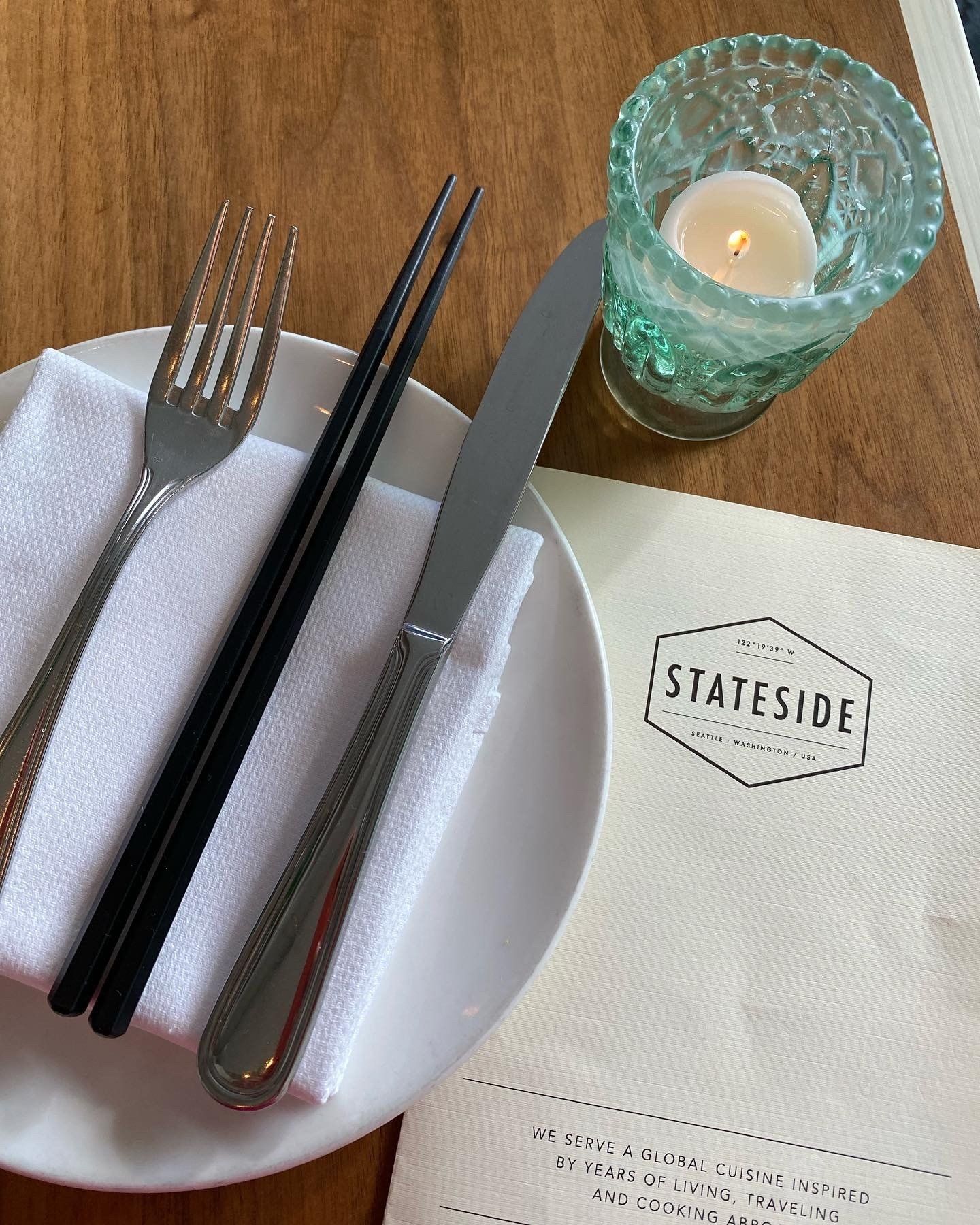 A plate with utensils and a candle on a placemat that says statside